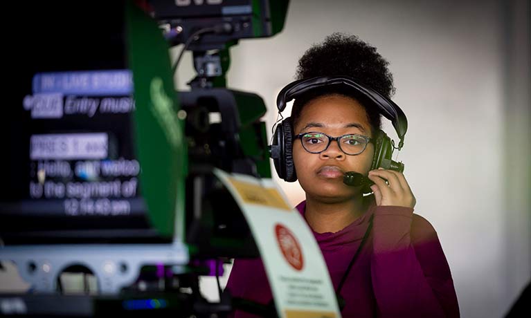 Female student in a TV studio working a camera. 