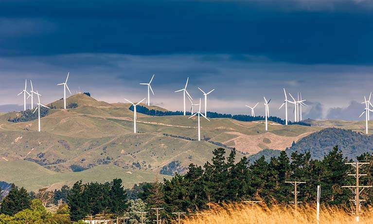 Hilly landscape covered with wind farm turbines with a dark cloudy sky in background