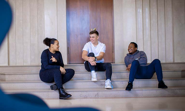 Three students sat on stairs inside a building