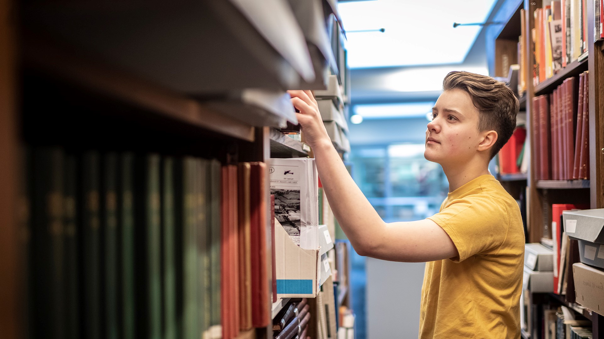 A student browsing textbooks in the CU London Dagenham library.