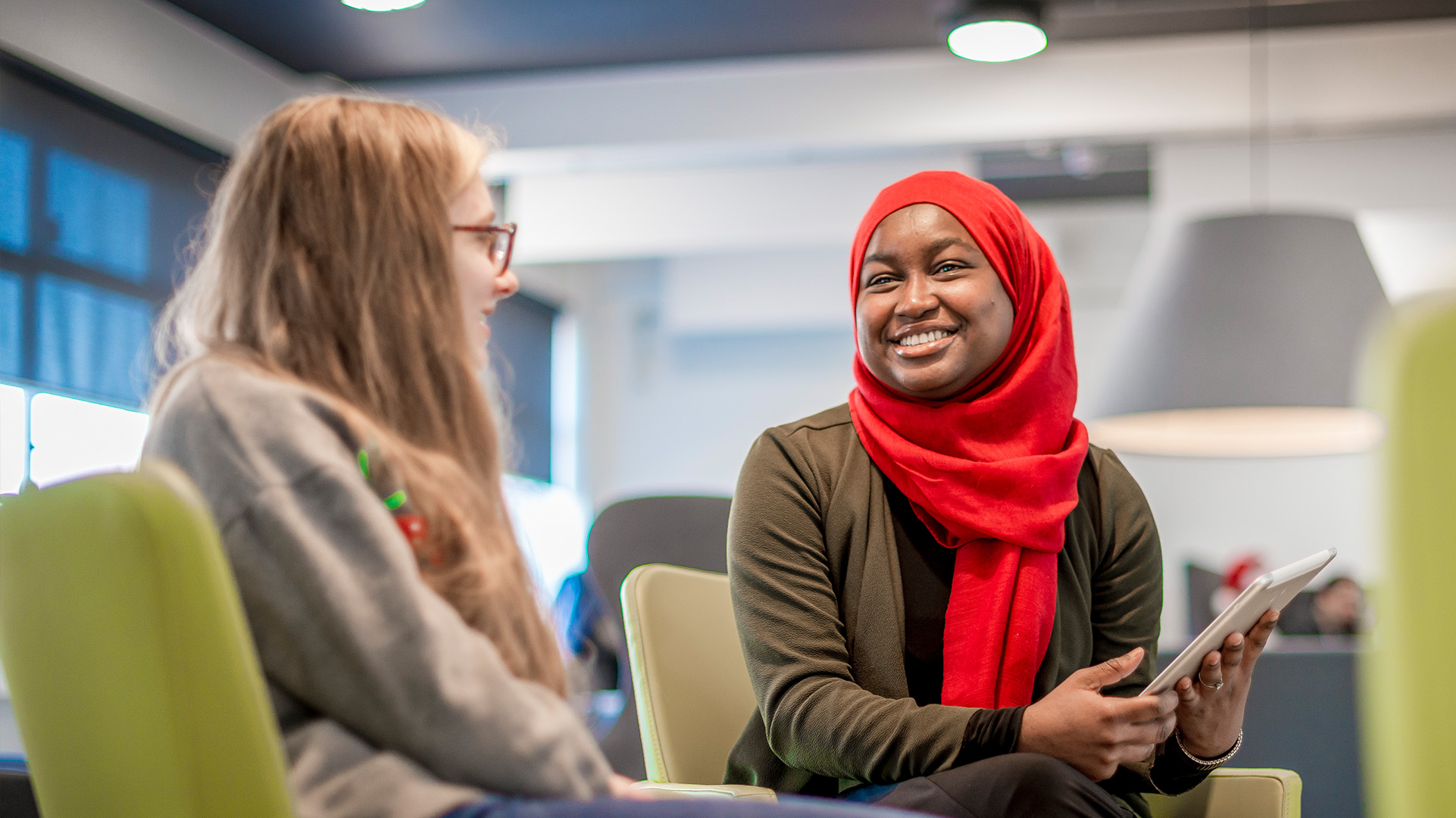 Young lady wearing a hijab smiling while talking to another young lady