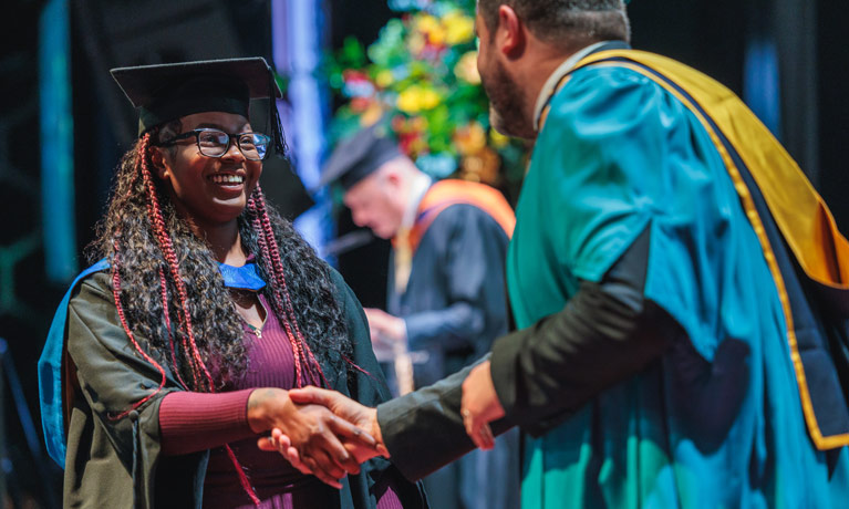A smiling student graduating from CUL Greenwich at a graduation ceremony.