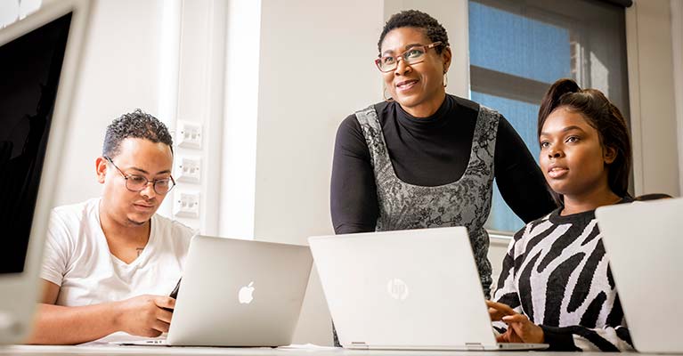 Lecturer stood over two students who are working on their laptops