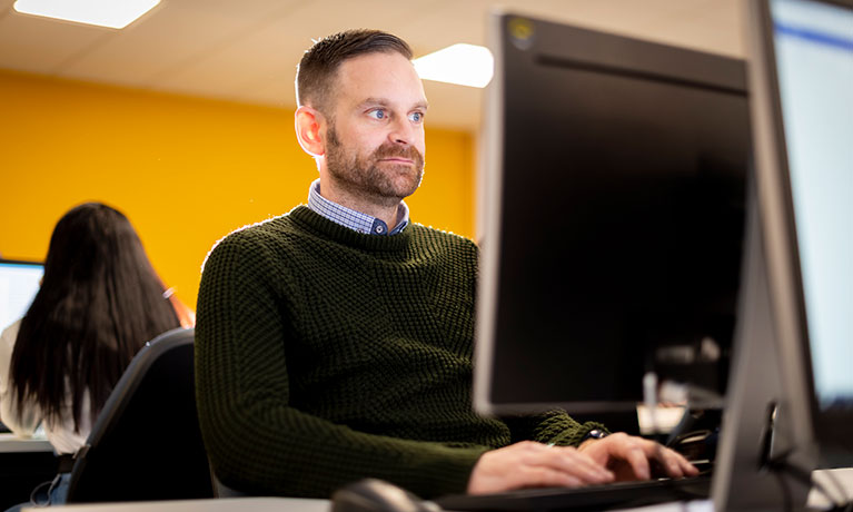 Male student sat in front of a computer typing