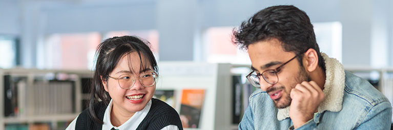 Two students talking and smiling while studying