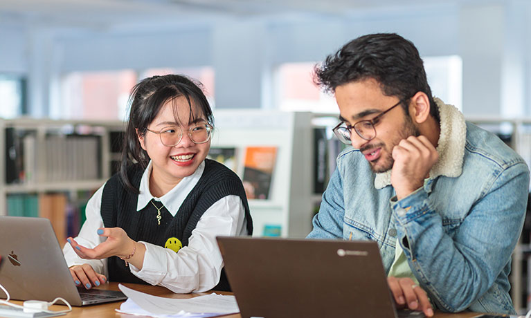 Two students smiling working on laptops