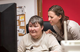 A nurse attending a patient who is using a desktop computer.