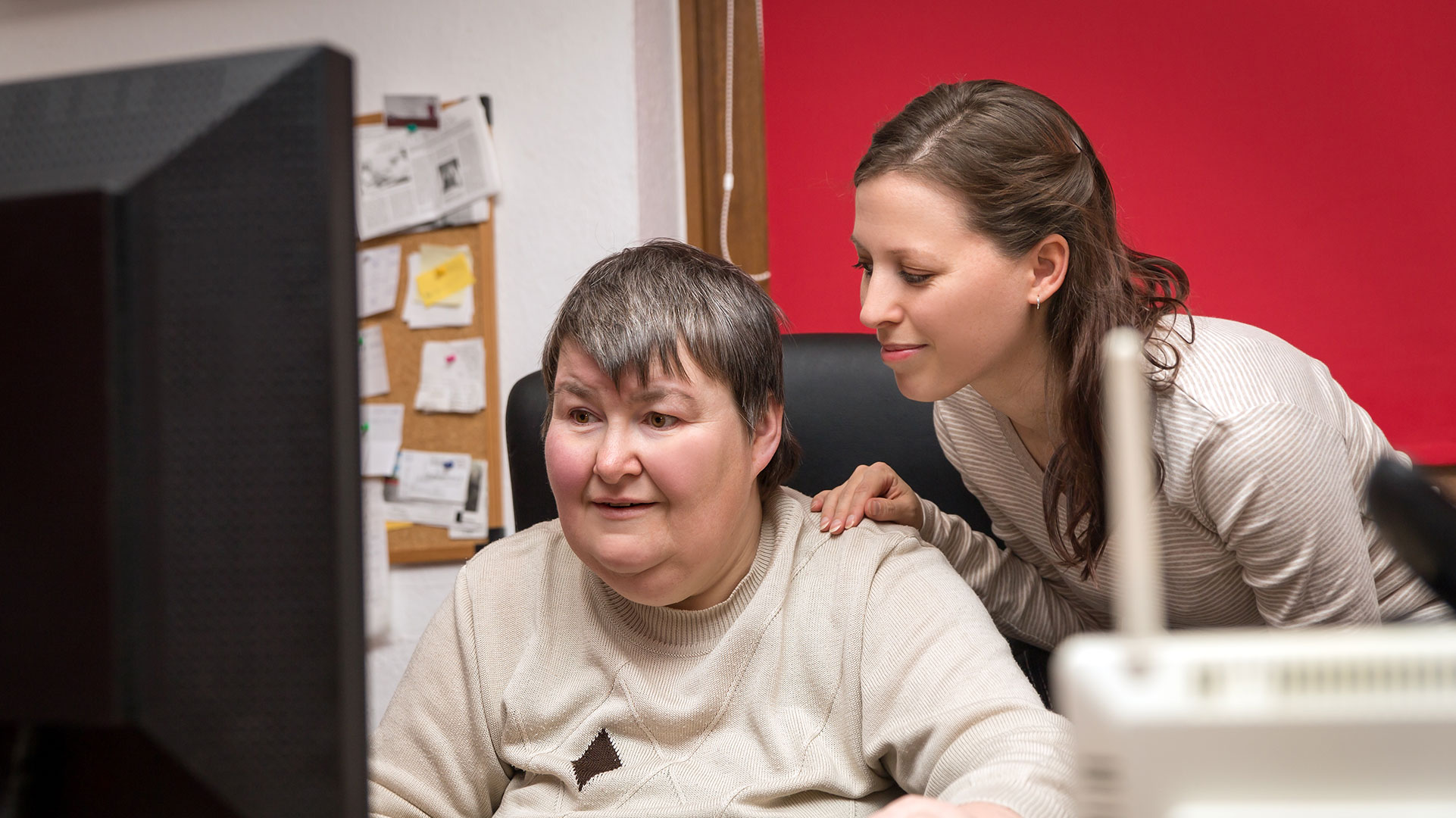 A nurse attending a patient who is using a desktop computer.