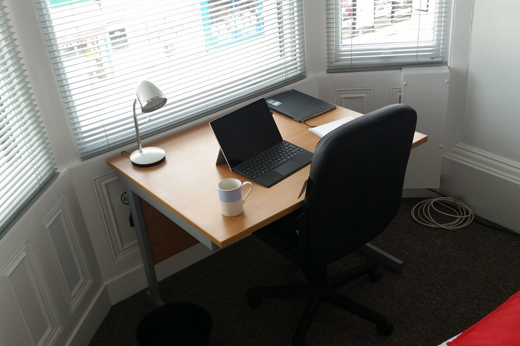 Small desk in front of a window with a laptop on and a desk chair pushed in against