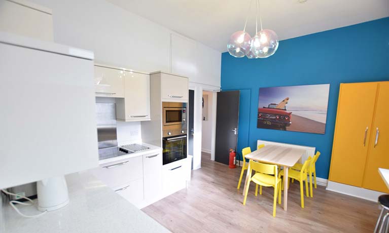 Open plan kitchen area with a small dining table againt a blue wall