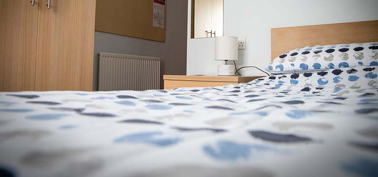 Close view of a bed alongside a bedside table with a lap and wardrobe