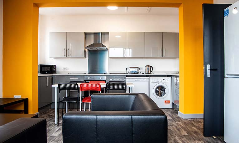 View of a living room with a yellow accent wall looking through to an open kitchen