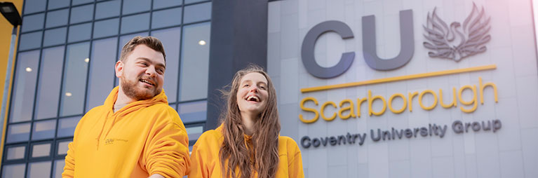 Two students wearing CUS sweatshirts smiling and standing outside CUS building