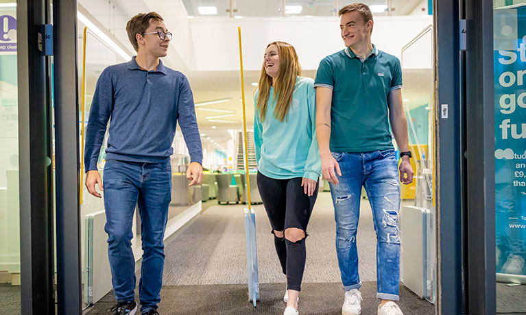 Three students talking whilst walking out of a building