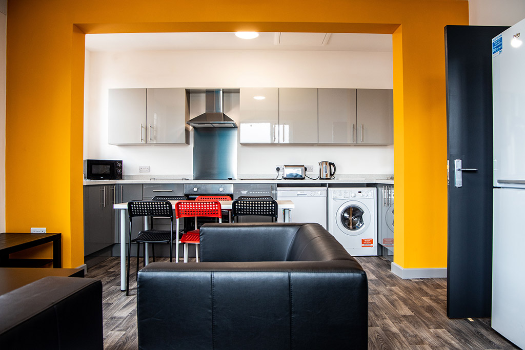 Open plan living room with a yellow accent wall through to kitchen area