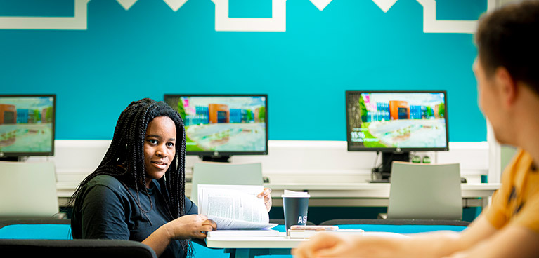 Woman in front of three screens talking to a man wearing yellow