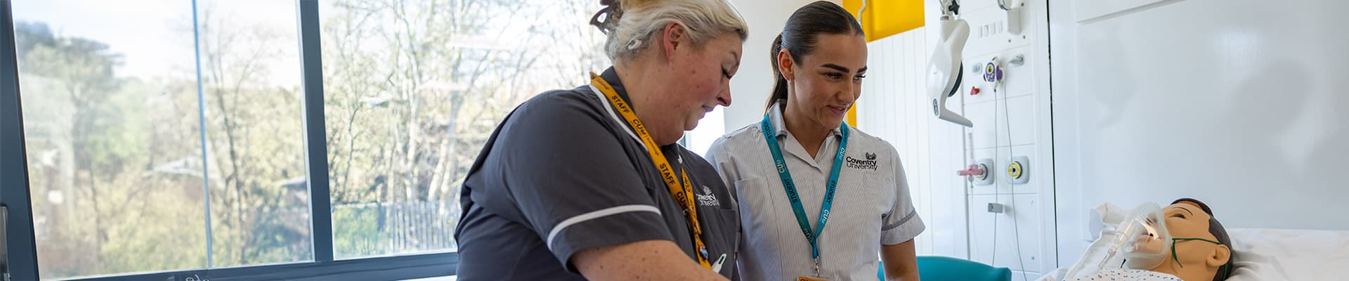 Student nurse stood over a manequin patient with another nurse