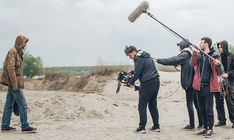 An actor and crew members filming on a beach