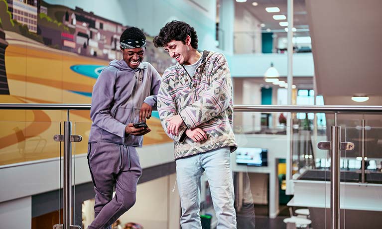 Two students leaning against a balcony looking at a phone