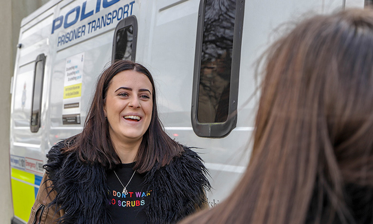 A CU Scarborough Policing student stands next to a police van