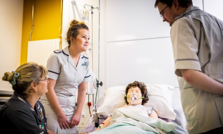 Three trainee nurses around a hospital bed 
