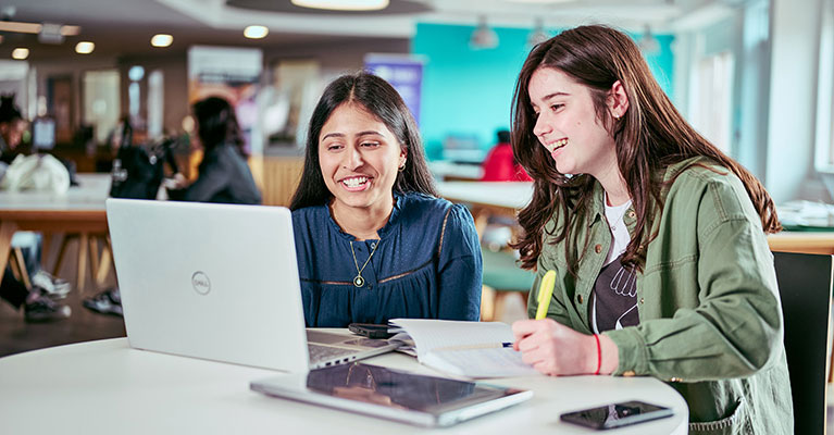 Two students sat at a table looking at a laptop