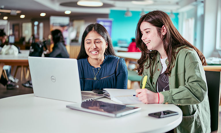 Two students sat at a desk looking at a laptop screen