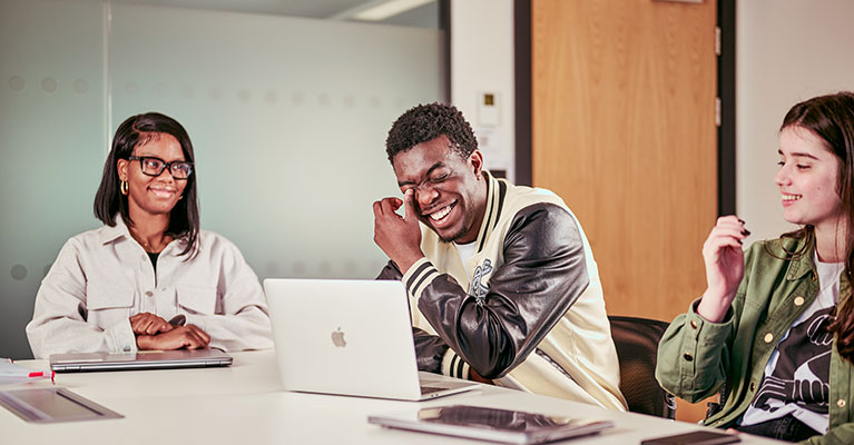 Three students sat at a desk laughing 