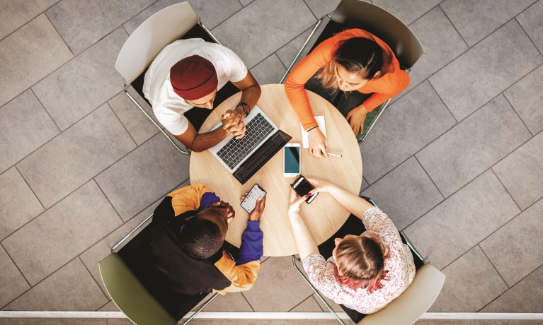 Four people sitting at a desk chatting