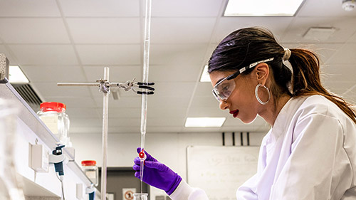 Student in a laboratory wearing a white lab coat and carrying out an experiment with long test tubes.