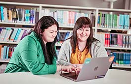 Two students sat together in a library looking at a laptop