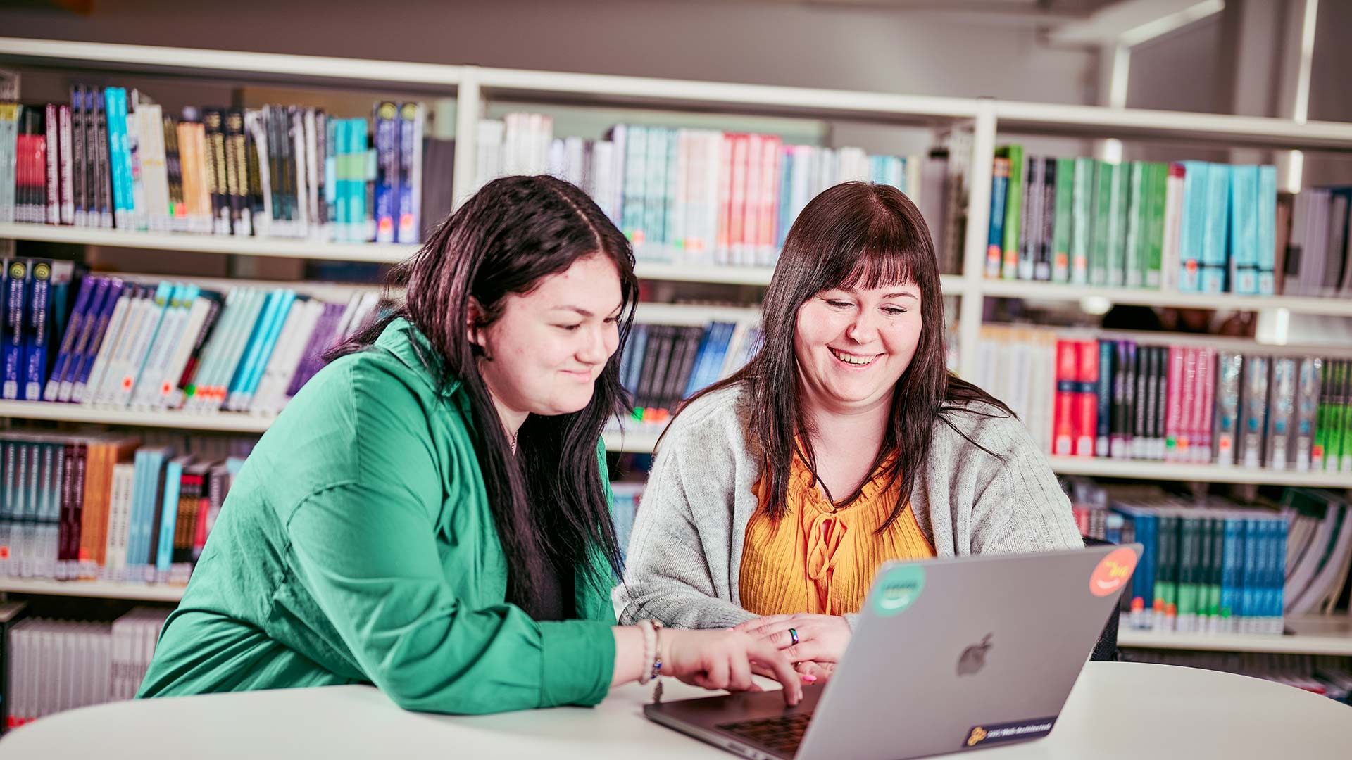 Two students sat together in a library looking at a laptop