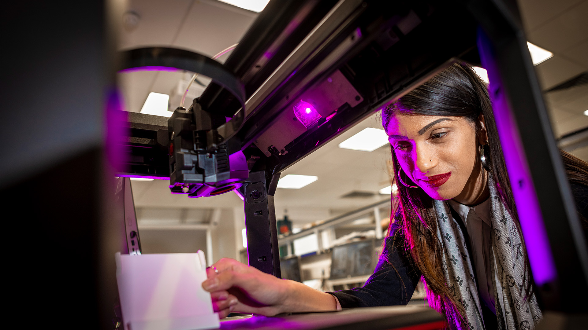 Young brunette woman looking at a 3D printer as it prints