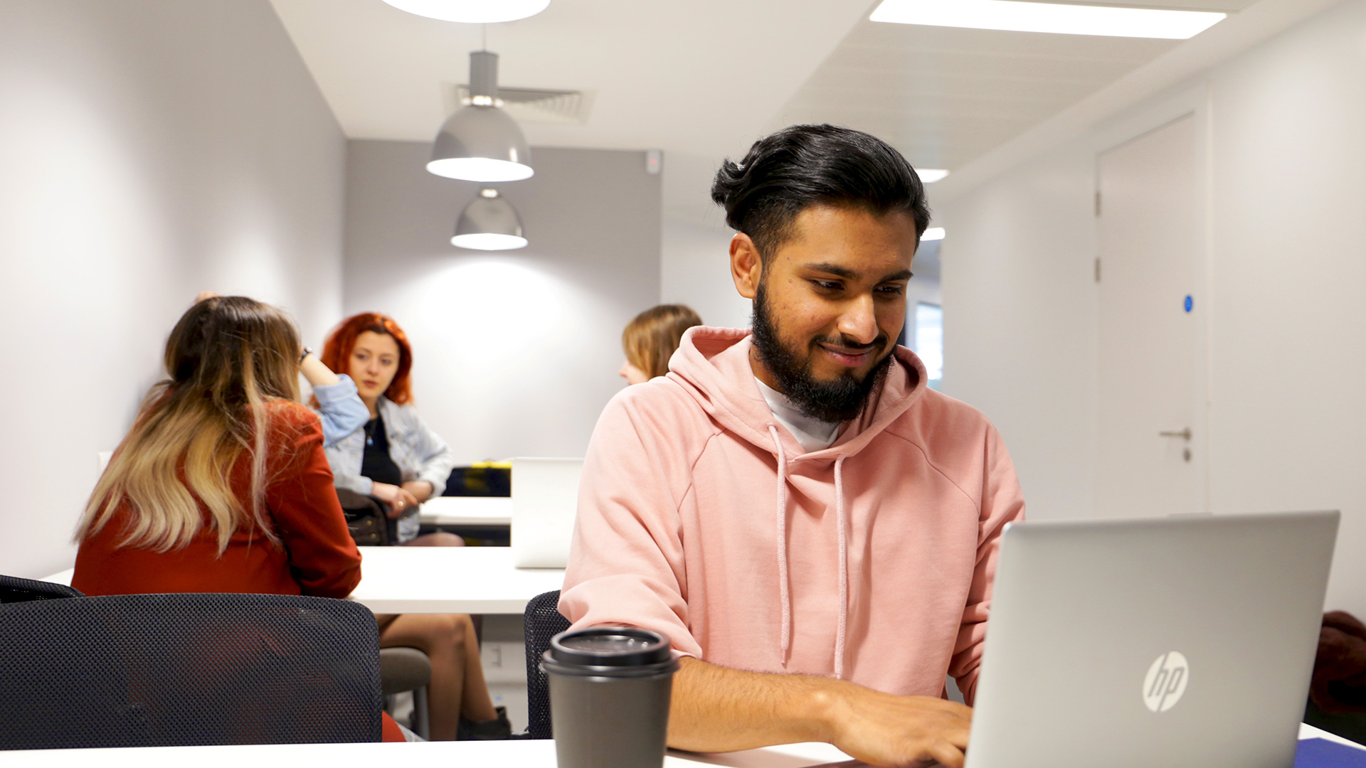 Student working on laptop with others talking behind