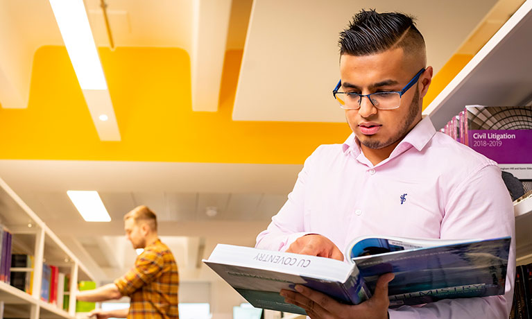 Male student reading a book in a library