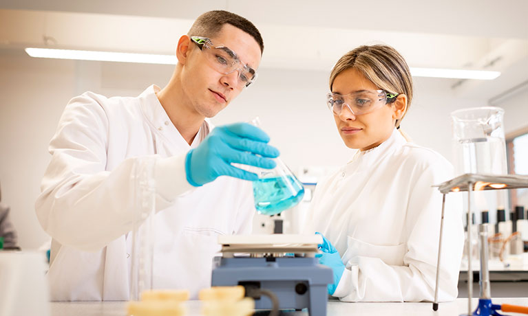 Two students wearing lab coats working in a lab environment