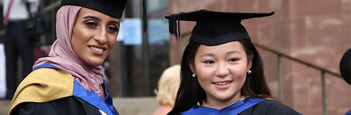 two graduates with gowns and hats looking at camera, smiling