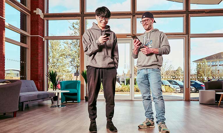 Two male students stood next to each other looking at their phones