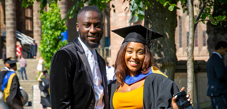 Student in graduation gown outside Coventry Cathedral ruins