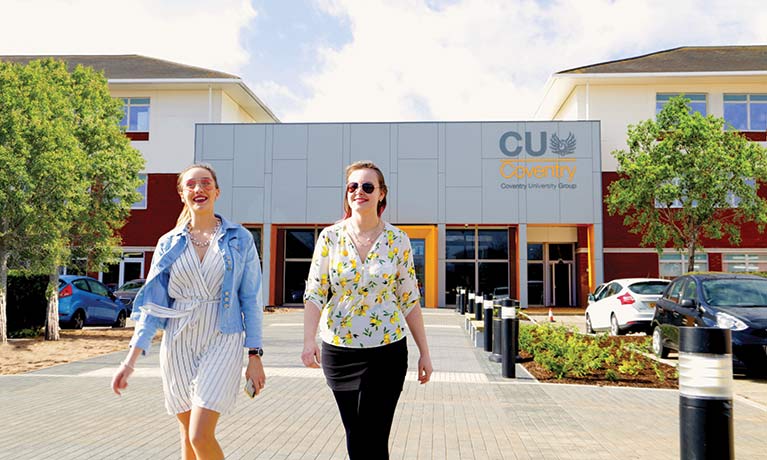 Two students walking outside with the CU Coventry building behind them.