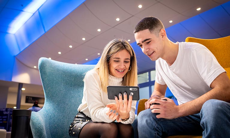 Students sitting in the student hub looking at a phone