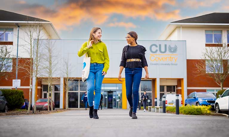 Two students talking whilst walking away from the CU Coventry building
