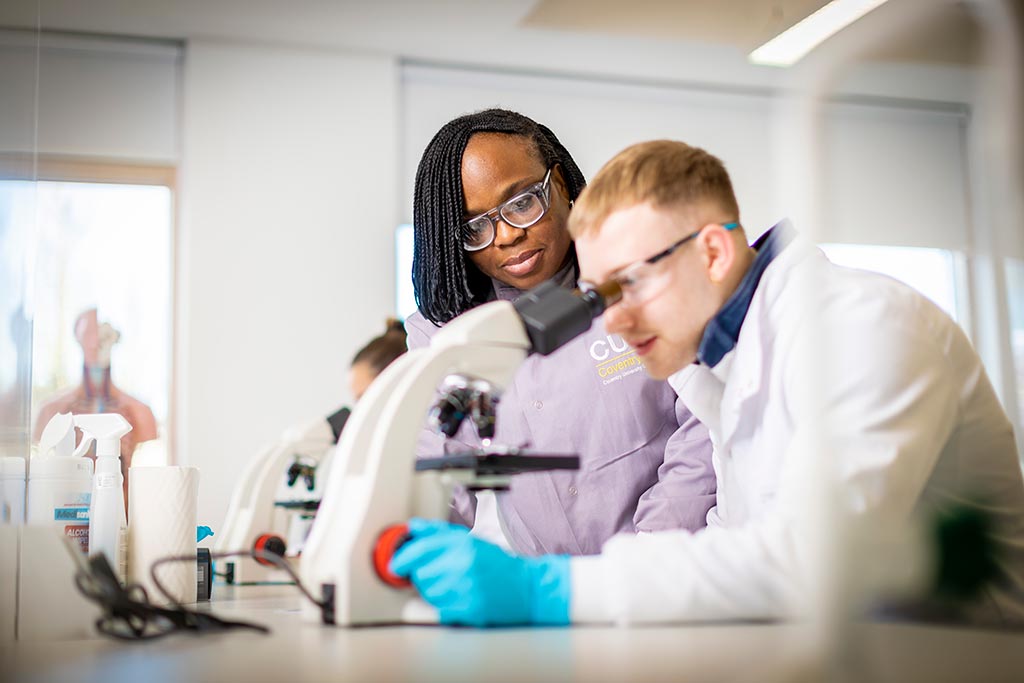 Two students in lab coats looking into a microscope