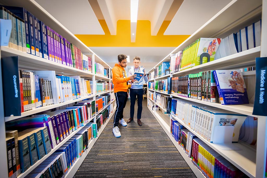 Two aisles of books with a student and lecturer stood at the end