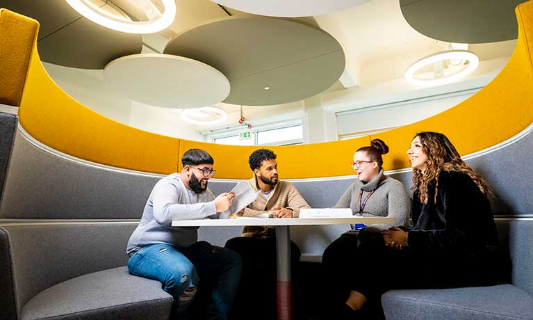 Group of students sat in a pod talking to each other