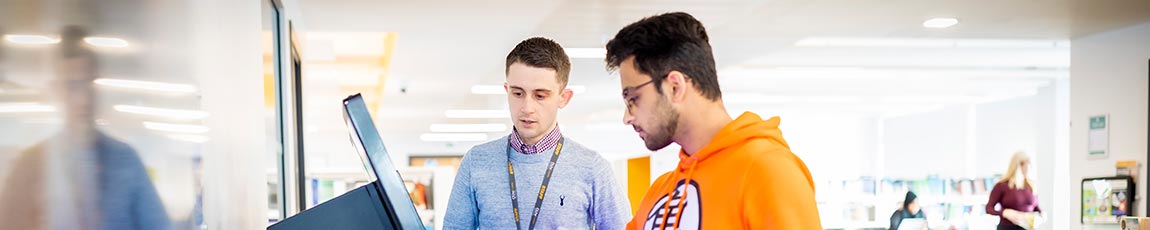 Lecturer standing with a student helping him on a digital screen