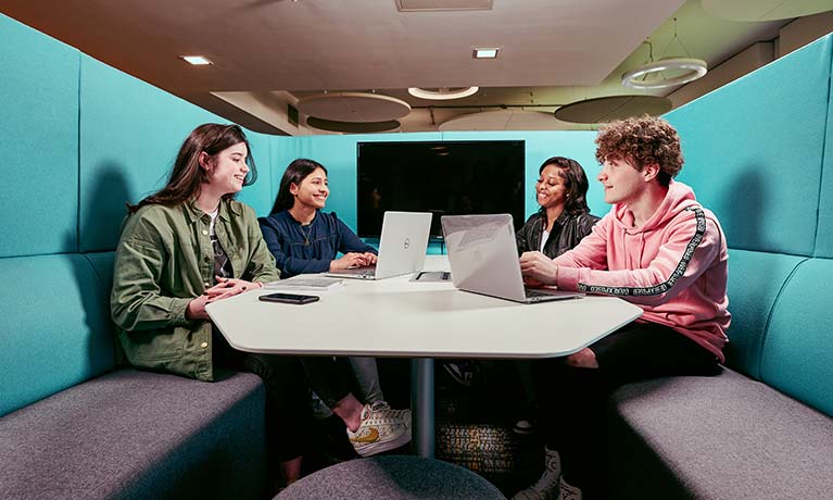 Four students working on their laptops sitting in a pod