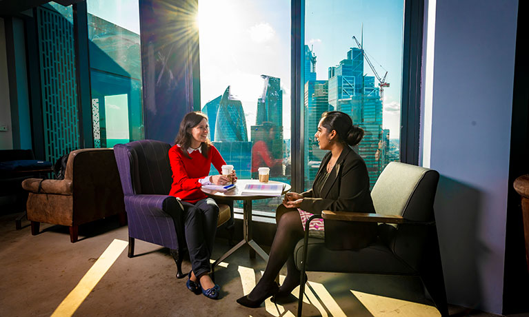 two women sitting in an office infront of the London skyline