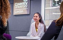 young female student chatting to two other students with the coventry university london sign on the wall in the background 