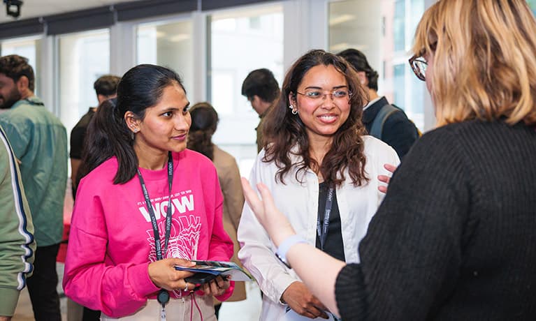 Two students having a conversation with a female in a busy room